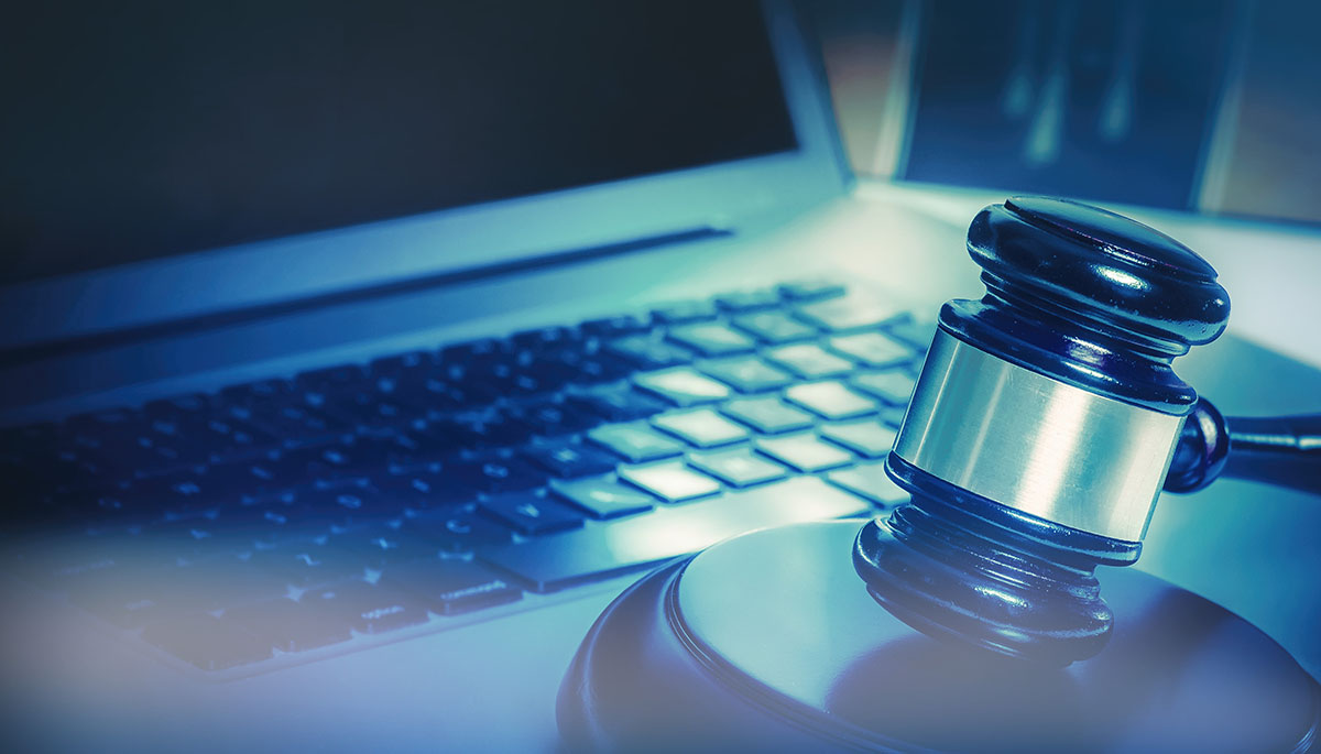 A wooden judge's gavel resting on its sound block beside an open laptop keyboard in cool blue light