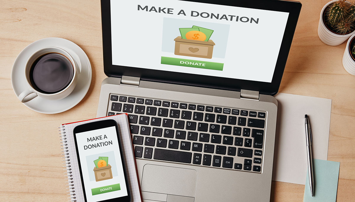 Overhead view of a laptop and a smartphone on a wooden desk, both showing a Make a Donation page with a green Donate button