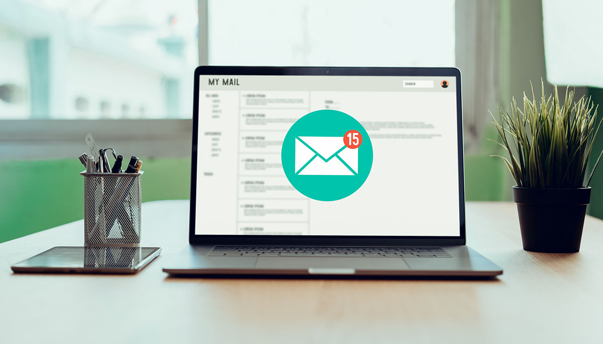 An open laptop on a wooden desk showing an email inbox with a mail icon and a notification badge reading 15