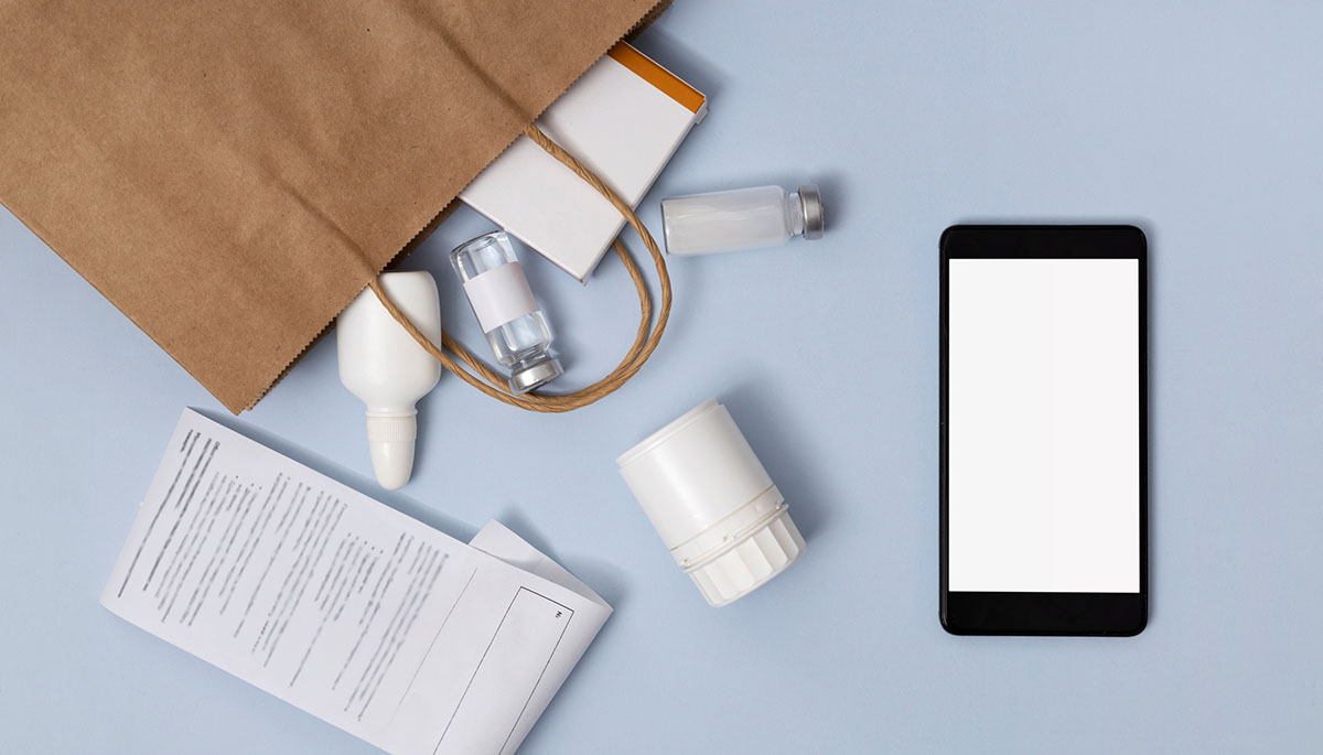 Overhead view of a brown paper pharmacy bag spilling medicine bottles and a box beside a printed receipt and a smartphone with a blank screen on a pale blue surface