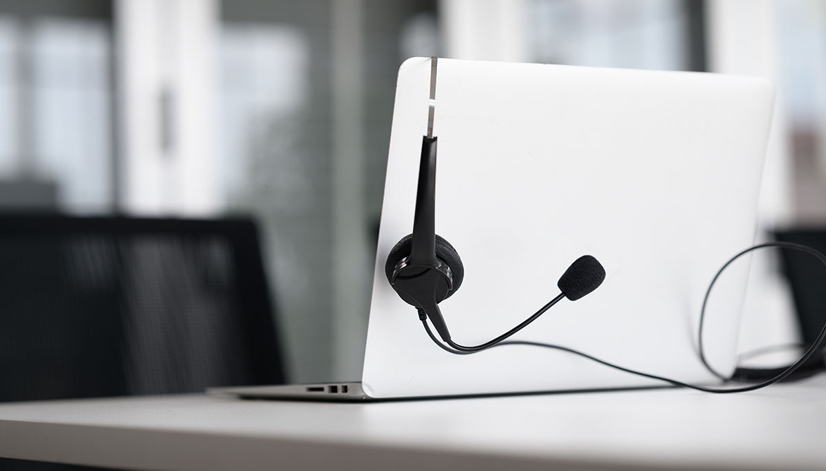A black call centre headset hanging on the lid of an open laptop on an empty office desk
