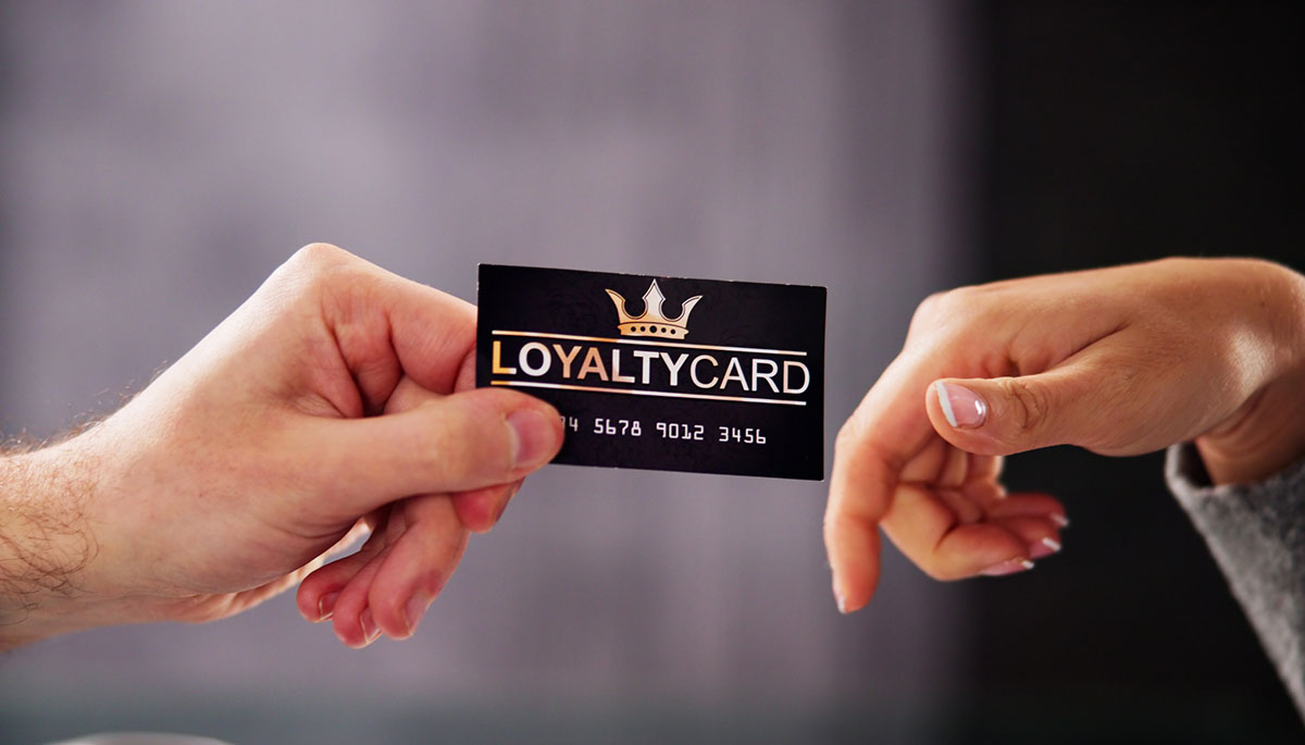 Close-up of one hand passing a black and gold loyalty card to another hand against a soft grey background